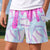 A person wearing light blue and white baseball-pattern shorts with dripping pink ice cream and sprinkle motifs, photographed outdoors on a baseball field.