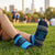 Person wearing marathon socks with NYC borough names on grass with a cityscape background