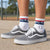 Gray Vans sneakers worn with white crew socks featuring a red, white, and blue USA design and a baseball graphic, shown on a person standing on a concrete surface outdoors.