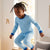 A two-piece children's pajama set featuring a long-sleeve top and matching pants. The pajamas are light blue with an all-over repeating pattern of red and black hockey figures, accented with solid blue trim on the collar, cuffs, and ankles.