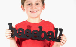 Black wooden baseball word sign held by a boy wearing a red t-shirt.