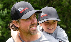 Father and son wearing matching black mesh trucker hats with "EAT. SLEEP. BASEBALL." embroidered text.