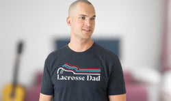 Man wearing charcoal gray Lacrosse Dad t-shirt with a colorful retro-style wave graphic and white text.