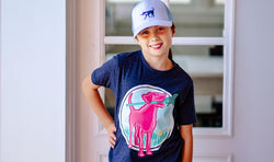 Girl wearing navy girls lacrosse t-shirt and hat featuring a pink dog holding a lacrosse stick.