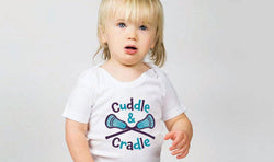 Child wearing white lacrosse baby onesie with "Cuddle & Cradle" text and a crossed lacrosse sticks graphic.