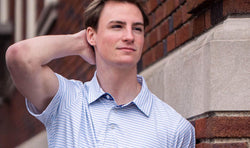 Youth wearing light blue and white striped lacrosse polo shirt with a subtle navy blue pattern inside the collar.