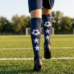 Person wearing navy socks with soccer ball and star patterns on a grassy field.