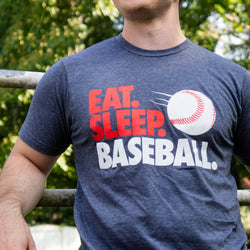 Model wearing navy baseball t-shirt featuring red and white "Eat Sleep Baseball" text and a flying ball graphic.