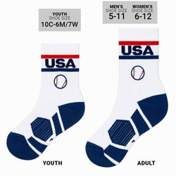A pair of white crew socks with navy blue and red athletic details, featuring 'USA' text and a baseball graphic on the cuff, displayed against a plain white background.