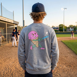 Person wearing a gray sweatshirt with an ice cream cone playing baseball design on a baseball field.