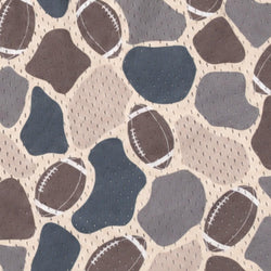 A close-up of a fabric pattern featuring brown and navy blue footballs mixed with abstract stone-like shapes in brown, gray, and beige.
