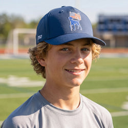 Boy wearing a blue usa themed cap with a dog design on a sports field.