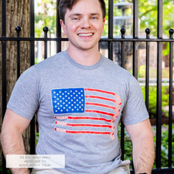 Man wearing a gray t-shirt with an American flag design, standing outdoors.