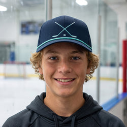 Person wearing a navy blue cap with a crossed hockey sticks design on an ice rink background