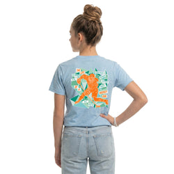 Person wearing a light blue t-shirt with a hockey girl graphic design on the back, standing against a white background.