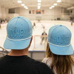 Two people wearing blue 'HOCKEY' caps in an indoor sports facility.