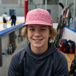 Person wearing a pink 'Hockey' cap on an ice rink