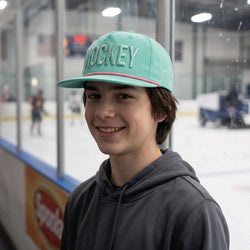 Person wearing a teal 'HOCKEY' cap in an indoor ice rink setting