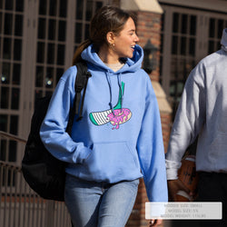 Person wearing a lightblue hoodie with a hockey donut graphic design, walking outdoors.