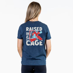 Person wearing a navy t-shirt with 'Raised in a Cage' graphic on the back
