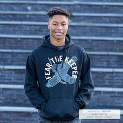Person wearing a navy hoodie with 'Fear The Keeper' graphic against a brick wall.
