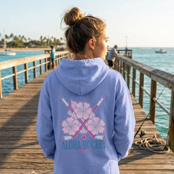 Person wearing a light blue hoodie with 'Aloha Hockey' design on a dock by the water.