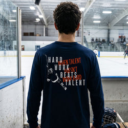 Person wearing a navy blue long-sleeve shirt with hockey motivational text and graphic at an ice hockey rink.