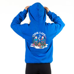 A person viewed from the back wearing a royal blue hoodie with a large graphic print on the back that reads 'ODR LIFE' above an illustrated campfire scene. The person is holding the hood up, and black leggings are visible against a plain white studio background.