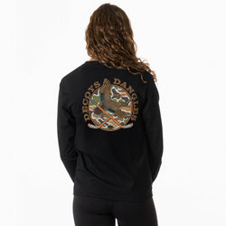 A girl viewed from behind wearing a black long sleeve t-shirt with a large graphic on the back. The graphic features the words 'DECOYS & DANGLES' in a tan font surrounding a camouflage-patterned circle with a duck and crossed hockey sticks