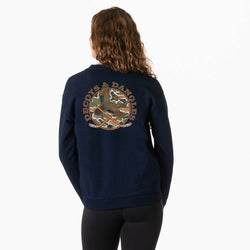 A girl viewed from behind wearing a navy blue sweatshirt with a large circular camouflage duck graphic with crossed hockey sticks and the words 'DECOYS & DANGLES' across the back, paired with black leggings against a plain white background.