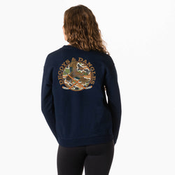 A girl viewed from behind wearing a navy blue sweatshirt with a large circular camouflage duck graphic with crossed hockey sticks and the words 'DECOYS & DANGLES' across the back, paired with black leggings against a plain white background.
