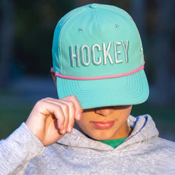 Person wearing a turquoise cap with 'HOCKEY' on it, outdoors.