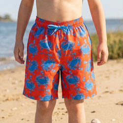 Person wearing red swim shorts with blue crab pattern on a beach
