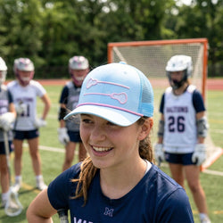 Girl in lacrosse uniform with cap on a field with teammates in the background