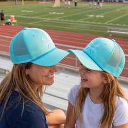 Woman and child wearing matching blue lacrosse caps on a track field