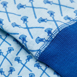 A close-up of a blue and white lacrosse patterned fabric of a pajama shirt, featuring a repeating blue axe motif on a white background with a solid blue ribbed cuff.