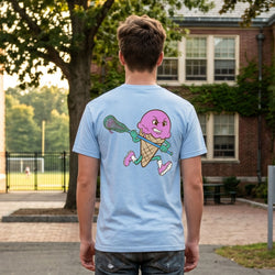Person wearing a light blue t-shirt with a colorful ice cream cone and lacrosse stick graphic on the back, standing outdoors.
