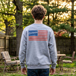 Person wearing a gray sweatshirt with a lacrosse flag design outdoors.
