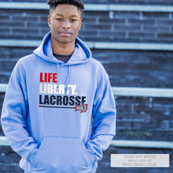 Person wearing a blue hoodie with 'LIFE LIBERTY LACROSSE' text and logo on a brick wall background.