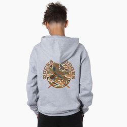 A child viewed from behind wearing a light heather gray hoodie with a large circular back graphic. The graphic features the words 'Ducks & Dodges' in brown around a camouflage-and-wood design, with crossed sticks at the bottom.