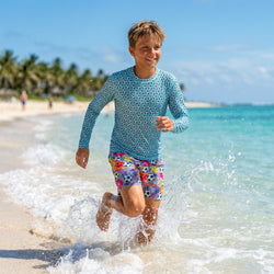 Child running on a beach wearing a blue soccer long-sleeve rash guard and colorful swim shorts.