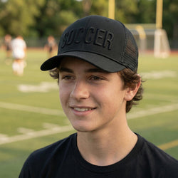 Person wearing a black cap with 'SOCCER' on a sports field