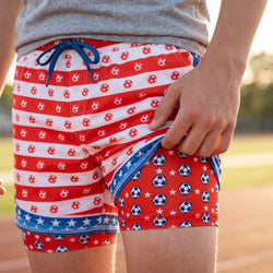 Person wearing red, white, and blue soccer patterned shorts with a blurred outdoor background