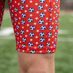 Red shorts with soccer ball and star pattern worn by a person on a grassy field.