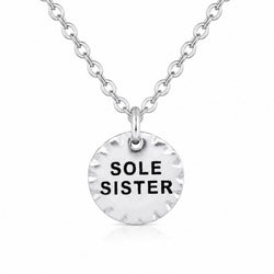 A silver disc pendant necklace with the words 'SOLE SISTER' engraved in black letters, suspended from a silver cable chain on a white background.