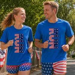 A man and a woman jogging outdoors, both wearing bright blue t-shirts with a large vertical 'USA' graphic in an American flag pattern and matching patriotic shorts.