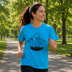 A woman jogging on a tree-lined path wearing a bright blue athletic t-shirt with a black graphic of a mountain, sun, and the text 'LIFE'S SHORT RUN LONG'.