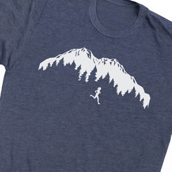 A close-up of a heather navy blue t-shirt featuring a white graphic print of a mountain range with pine trees and a small running figure.