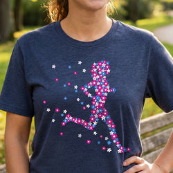 A woman wearing a navy blue heathered t-shirt with a colorful running silhouette made of pink, blue, and white flowers, set against a blurred outdoor background.