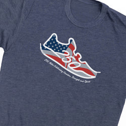 A close-up of a heather navy t-shirt featuring a graphic of a sneaker filled with an American flag design (stars and stripes) and the text '250 Miles Celebrating Freedom, Strength and Spirit' printed below it.